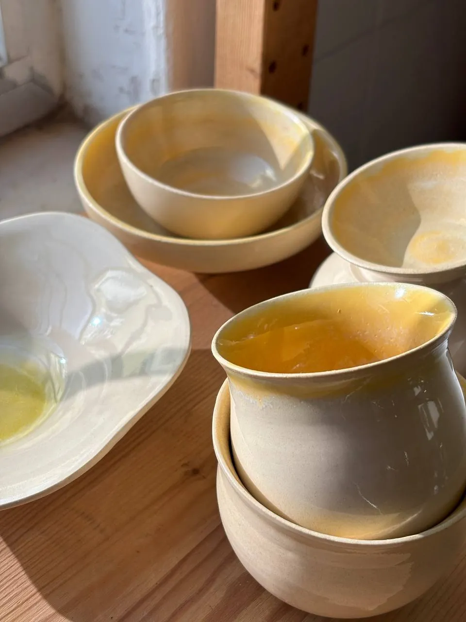 Taças e canecas com vidrado amarelo, empilhadas ao sol.