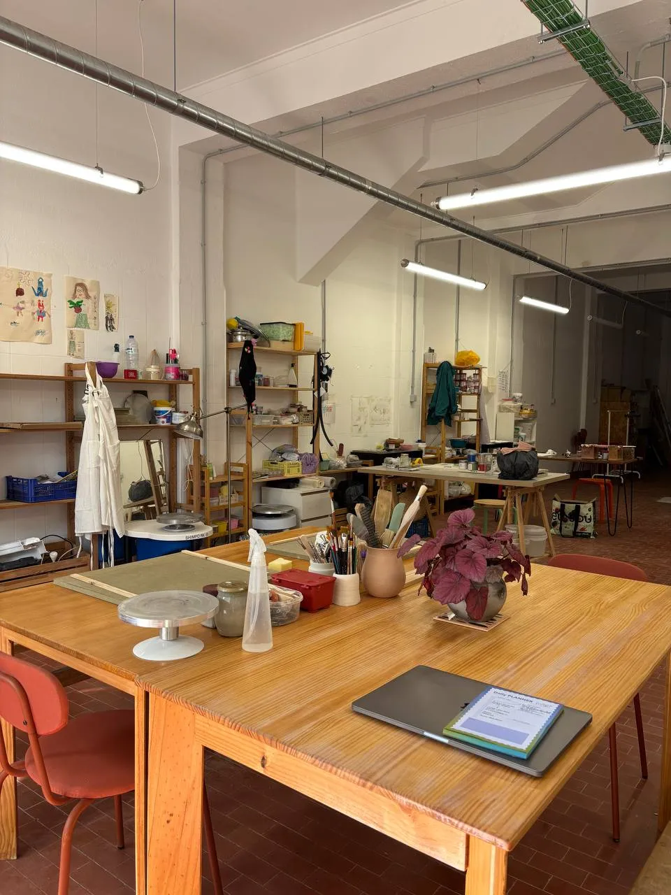 O atelier: bancadas de madeira, a roda de oleiro, prateleiras de ferramentas.
